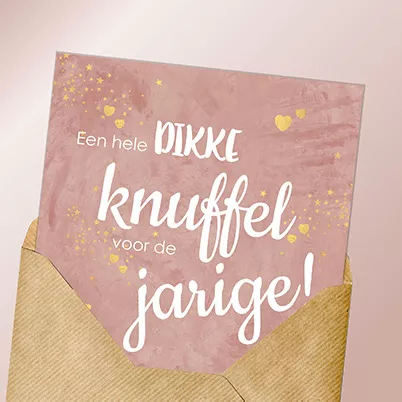 Roze verjaardagskaart met gouden hartjes en de tekst ‘Een hele dikke knuffel voor de jarige’, in een kraft envelop.